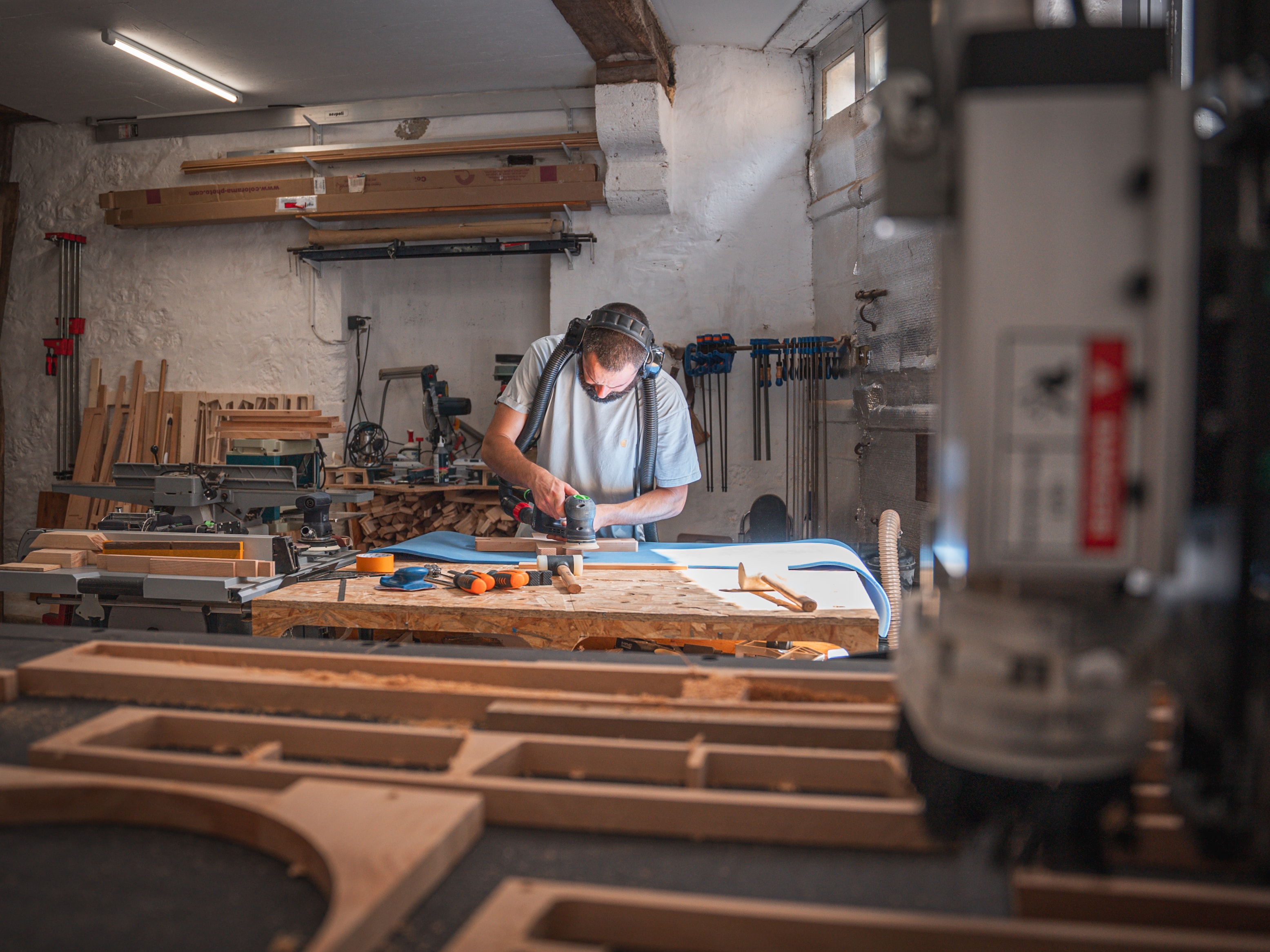 Haddock Menuiserie carpenter sanding wood in his workshop in France and CNC in the foreground