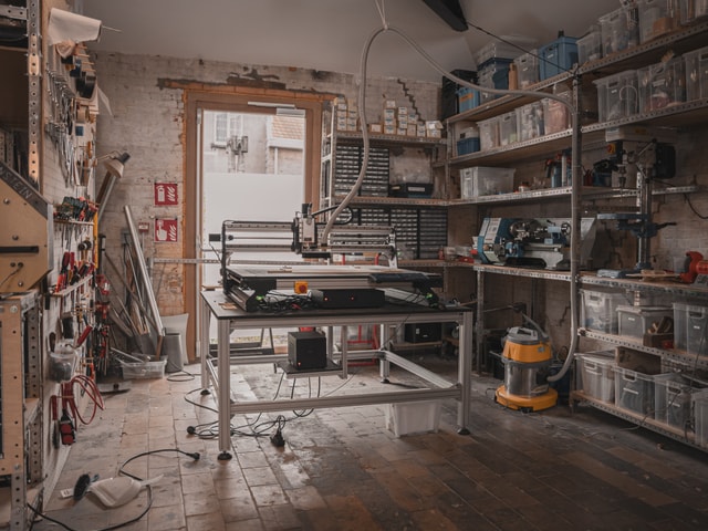 Mekanika Pro CNC machine front view installed in a workshop with a vacuum connected and plastic boxes on the side
