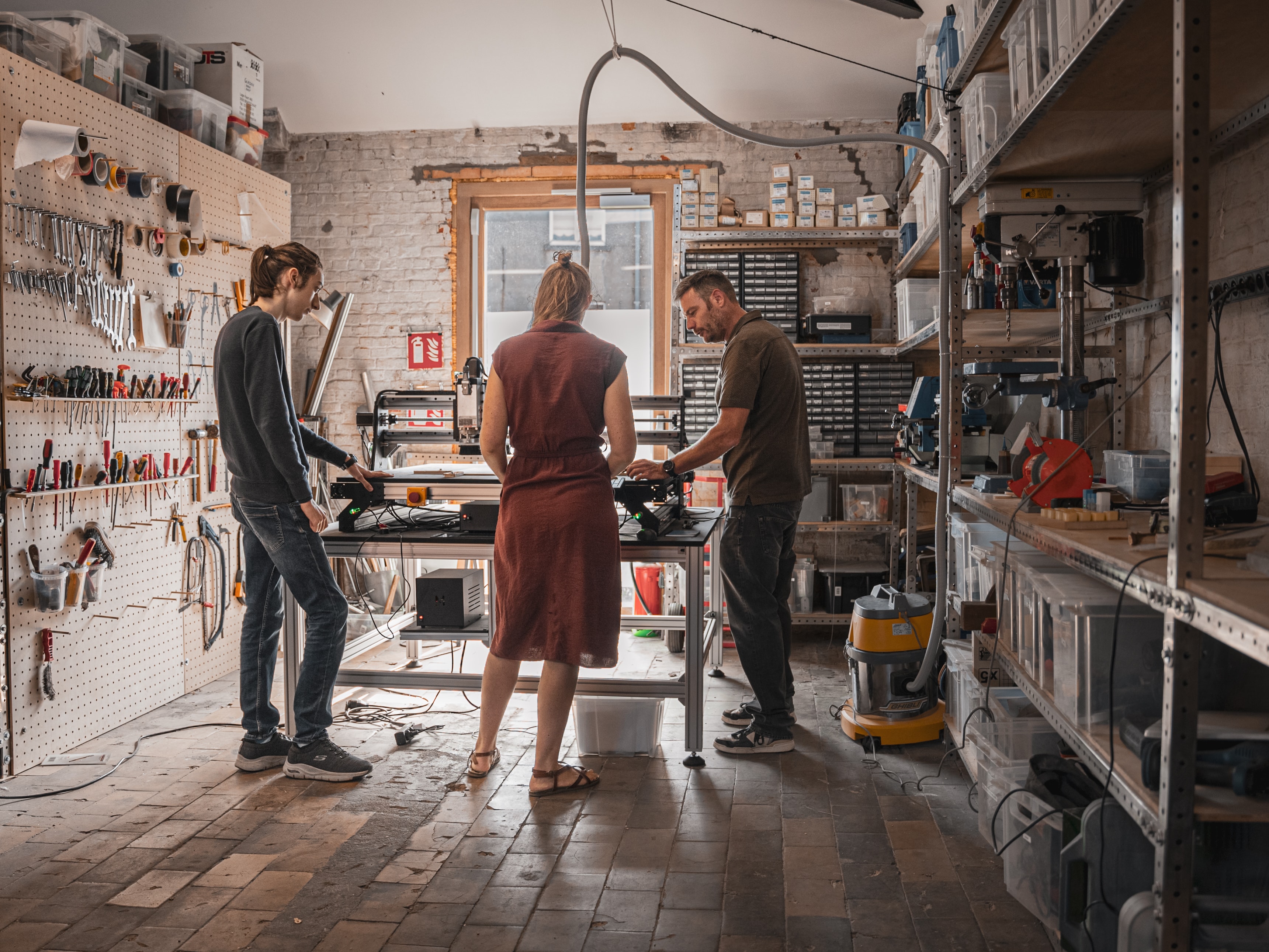 3 Fab lab members surounding a CNC milling machine in a workshop filled with tools and boxes