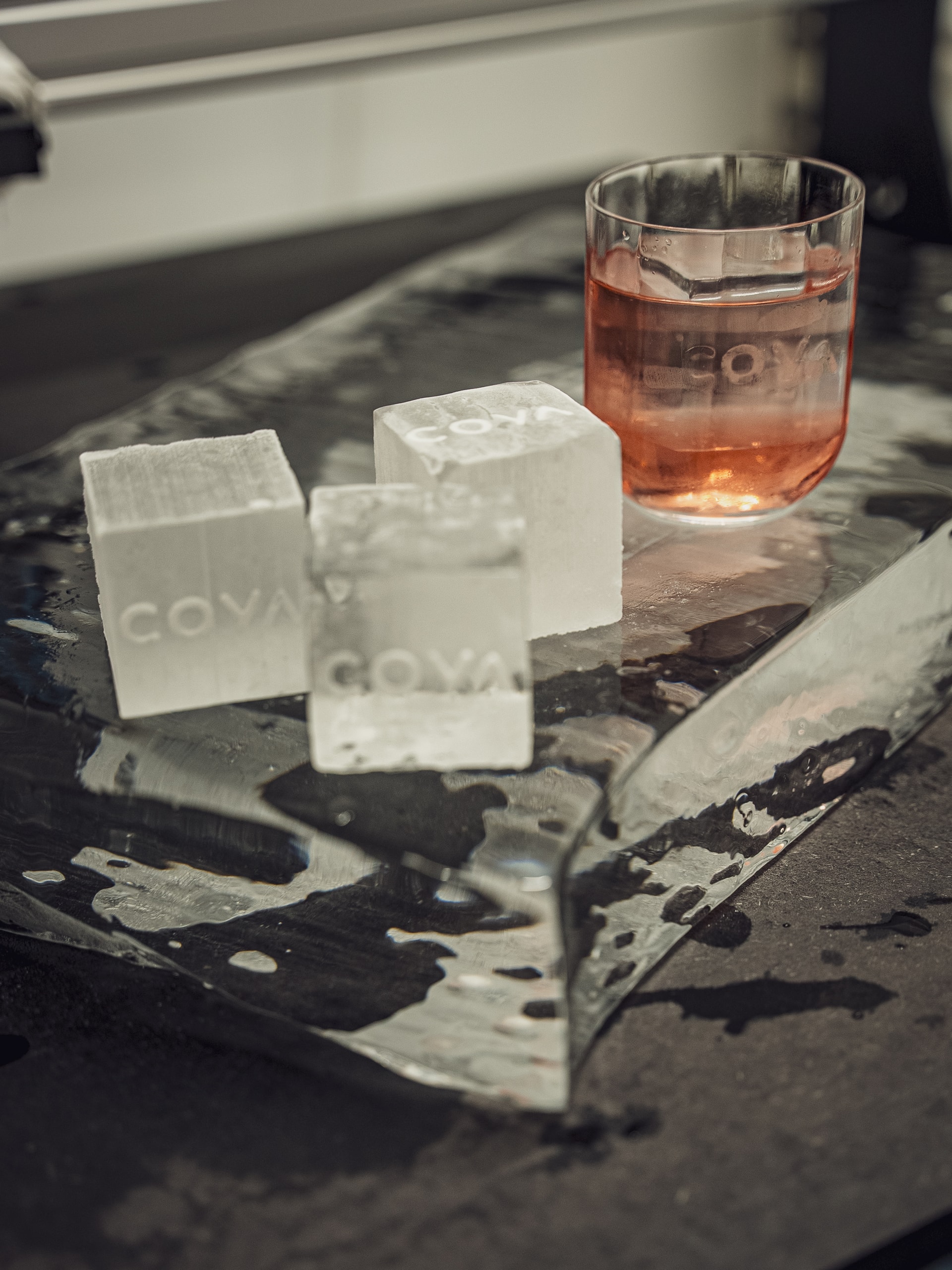 Ice slab with customised ice cubes with brand engraved in it and a cocktail glass in the background